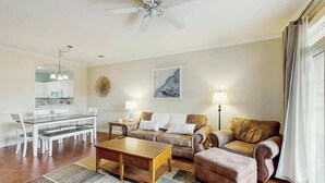 Uma sala de estar com área de jantar, ventilador de teto, um quadro e uma luminária.