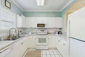 Eine Küche mit weißen Schränken, einer Mikrowelle, einem Backofen, einer Spüle und einem Kühlschrank.