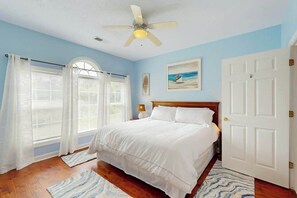 Ein Schlafzimmer mit einem Bett, einem Deckenventilator, einer Tür und einem Fenster mit Vorhängen.