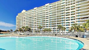 Um hotel com uma piscina grande, várias varandas e palmeiras.