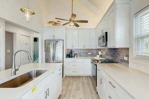 A modern kitchen with white cabinetry, stainless steel appliances, and a ceiling fan. - Lakefront Retreat at Litchfield by the Sea (Pawleys Island)
