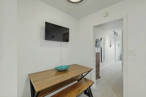 A room with a wooden table, a bowl, a flat-screen TV mounted on the wall, and a hallway leading to another room. - La Mirage Unit 402 Condo (Myrtle Beach)