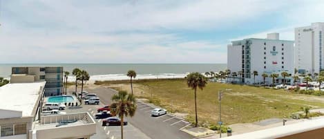 A hotel with a view of the ocean, parking area, and a building with a sign.