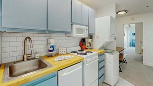Uma cozinha compacta com pia, fogão, micro-ondas e armários brancos.