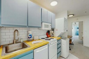 A compact kitchen with a sink, stove, microwave, and white cabinets. - La Mirage Unit 402 Condo (Myrtle Beach)