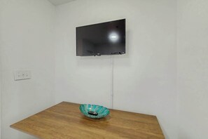 A room with a mounted flat-screen TV on the wall, a wooden table, and a decorative bowl on the table. - La Mirage Unit 402 Condo (Myrtle Beach)
