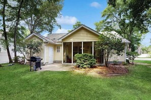 A single-story house with a covered porch, a small front yard, and a grill in the yard. - Pawleys Beach Retreat (Pawleys Island)
