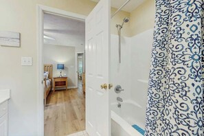 Ein Badezimmer mit Dusche, einer Tür zu einem Schlafzimmer und einem gemusterten Vorhang.