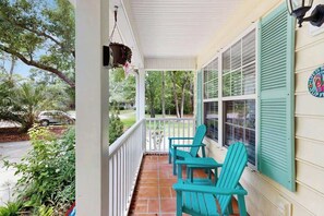 A porch with two chairs, a hanging planter, and a view of the street. - Pawleys Beach Retreat (Pawleys Island)