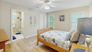 Ein Schlafzimmer mit einem Bett, einem Deckenventilator, einem Nachttisch und einem Fenster mit Jalousien.