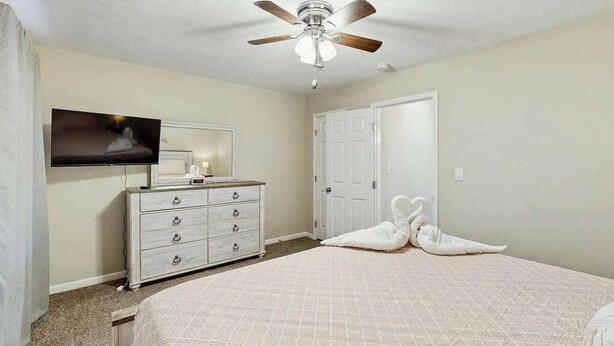 A bedroom with a bed, a dresser, a television, a ceiling fan, and a door. - Whalecome Inn Retreat (Myrtle Beach)