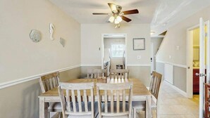A dining area with a wooden table and chairs, a ceiling fan, and a door leading to another room. - Whalecome Inn Retreat (Myrtle Beach)