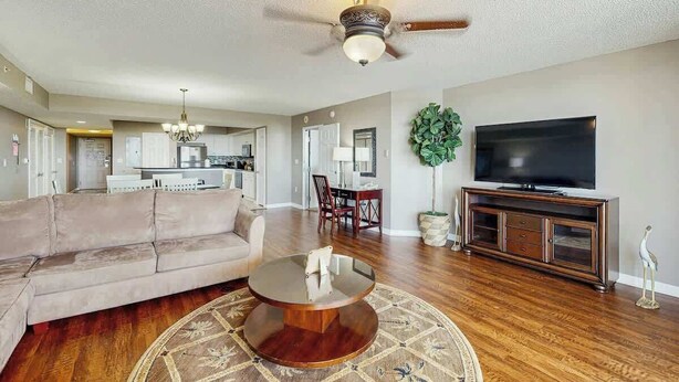 A living room with a sofa, coffee table, TV, and a ceiling fan. - Yacht Club Villas 2-702 (North Myrtle Beach)