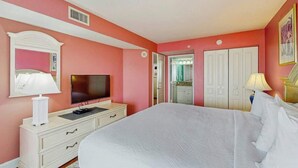 Ein Schlafzimmer mit Bett, Fernseher, Kommode und einer Tür zu einem Badezimmer.