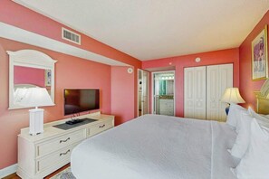 Ein Schlafzimmer mit Bett, Fernseher, Kommode und einer Tür zu einem Badezimmer.