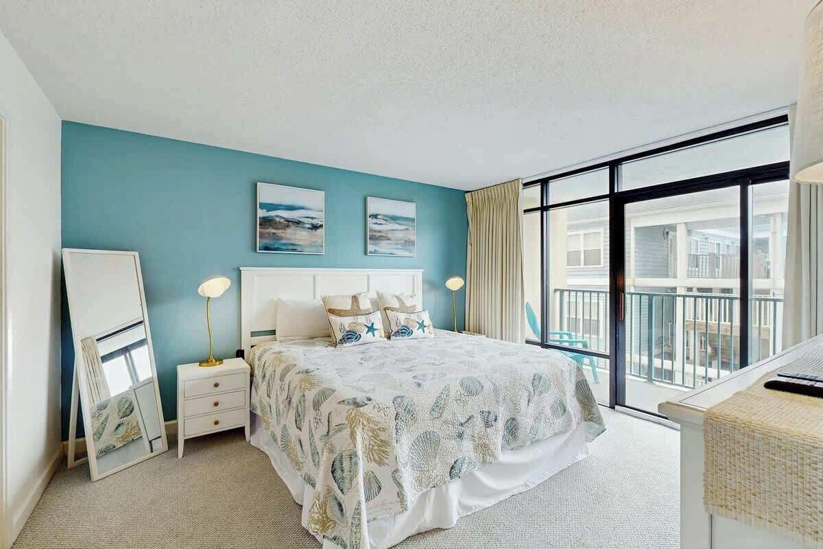Une chambre avec un grand lit, une table de chevet, un miroir et une vue sur le balcon extérieur.