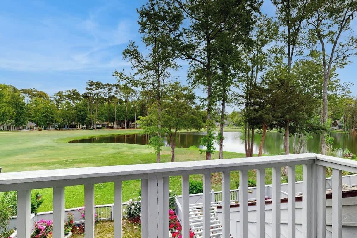 Blick von einer Terrasse auf einen Golfplatz mit Teich, umgeben von Bäumen und blauem Himmel.