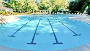 Ein klares Schwimmbecken mit mehreren Bahnen, umgeben von Liegestühlen und Sonnenschirmen.