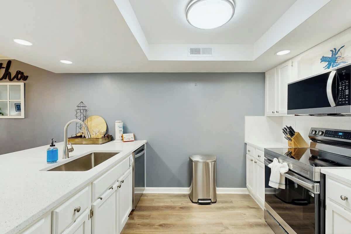 A modern kitchen with white cabinetry, a stainless steel sink, a microwave, and an oven.