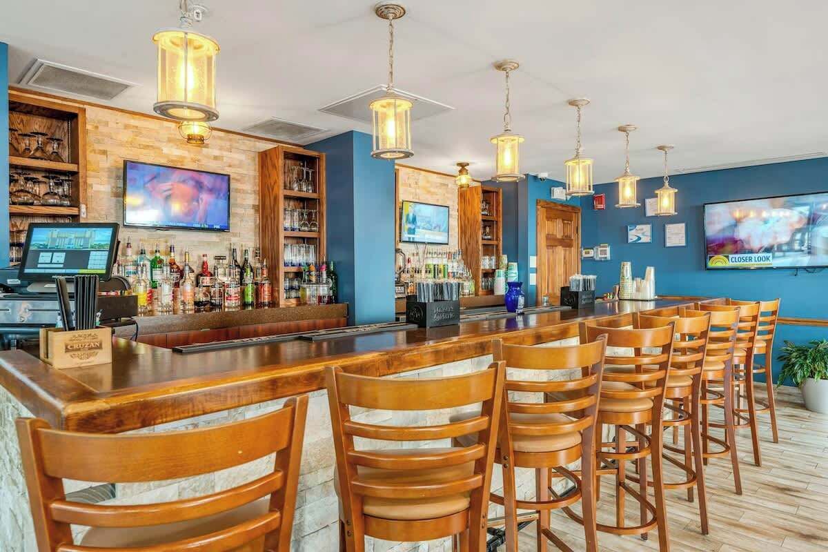 Zona de bar con taburetes de madera, una barra con caja registradora y estanterías llenas de botellas.