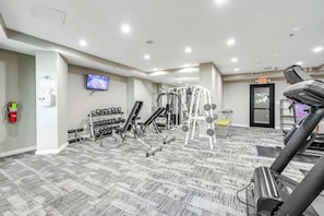 Ein Fitnessraum mit verschiedenen Trainingsgeräten, einem an der Wand montierten Fernseher und einem Feuerlöscher.