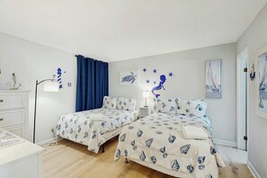 A bedroom with two beds, a desk, a dresser, and a nightstand with a lamp. - Holiday Towers Unit 205 (Myrtle Beach)