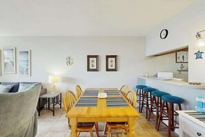 A dining area with a wooden table, chairs, and a bar counter with stools. - Holiday Towers Unit 205 (Myrtle Beach)