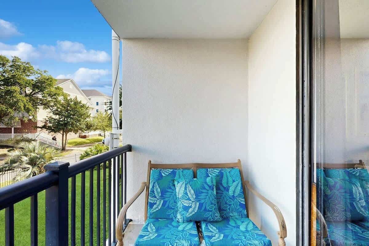 Ein Balkon mit einem Holzstuhl, einem Kissen, einer Glastür und Blick auf eine Wohngegend.