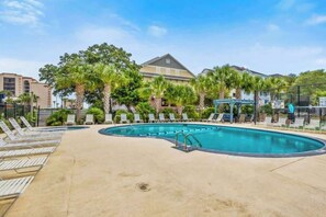 A swimming pool with lounge chairs and palm trees. - Holiday Towers Unit 205 (Myrtle Beach)