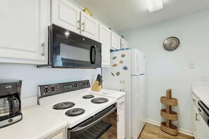 Eine Küche mit weißen Schränken, einer Mikrowelle, einem Herd und einem Kühlschrank.