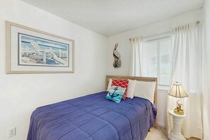 Une chambre à coucher avec un lit, un tableau, une lampe et une fenêtre avec des rideaux.
