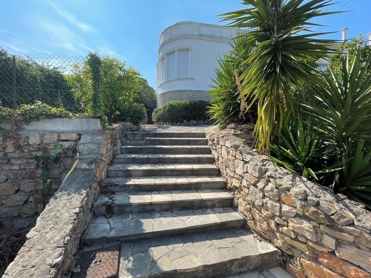 A set of stone steps leading up to a building with a rounded corner and a window with shutters.