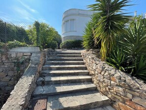A set of stone steps leading up to a building with a rounded corner and a window with shutters.