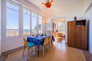 Uma sala de jantar com mesa posta para quatro pessoas, grandes janelas e um armário de madeira.
