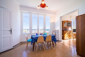 A dining area with a table set for four, a view of the sea through large windows, and a wooden cabinet in the background.