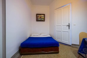 A small, narrow room with a single bed, a door, and a framed picture on the wall.