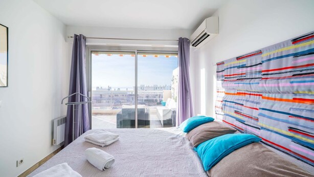 Ein Hotelzimmer mit einem großen Bett, Blick auf die Stadt und einem farbenfrohen, abstrakten Gemälde an der Wand.