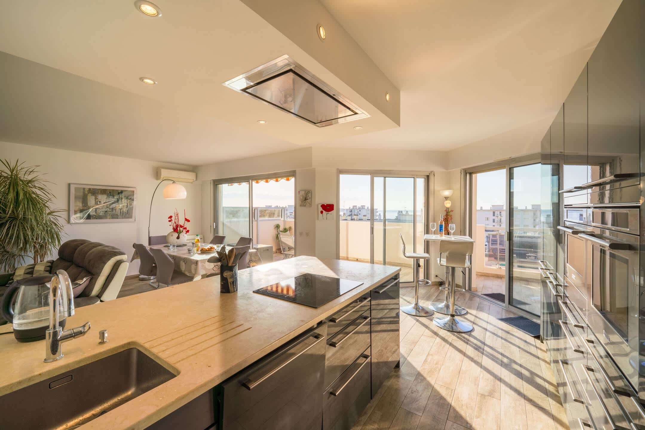 A modern kitchen with a central island, a dining area with chairs, and a view of the city through large windows.