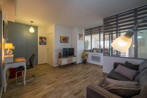 Ein modernes Wohnzimmer mit einer Couch, einem Fernseher, einem Schreibtisch und einer Lampe.