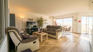 Ein Wohnzimmer mit Sofa, Sessel, Couchtisch, Fernseher und einer Topfpflanze.
