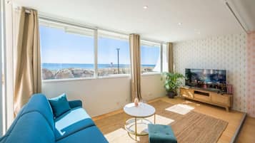Een moderne woonkamer met een groot raam, een bank, een klein rond tafeltje, een televisie en een potplant.