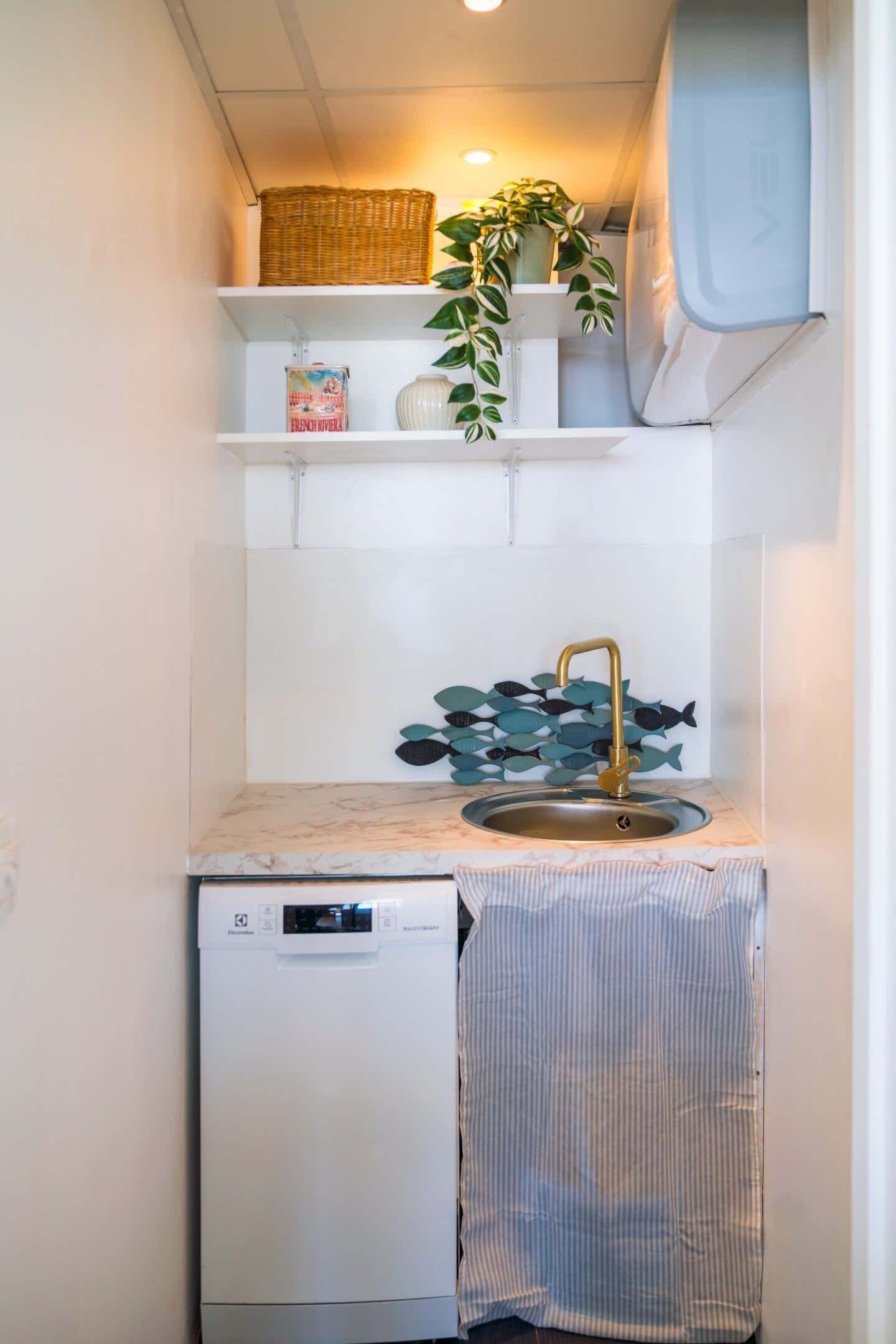 Een compacte kitchenette met een spoelbak, een kleine koelkast en een plantje op een plank.