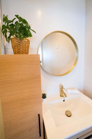 Une salle de bain avec un lavabo blanc, un robinet doré et un miroir rond doté d’un cadre doré.