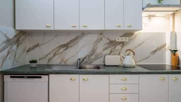 A kitchen with marble backsplash, white cabinets with gold handles, a built-in dishwasher, and a kettle on the counter.