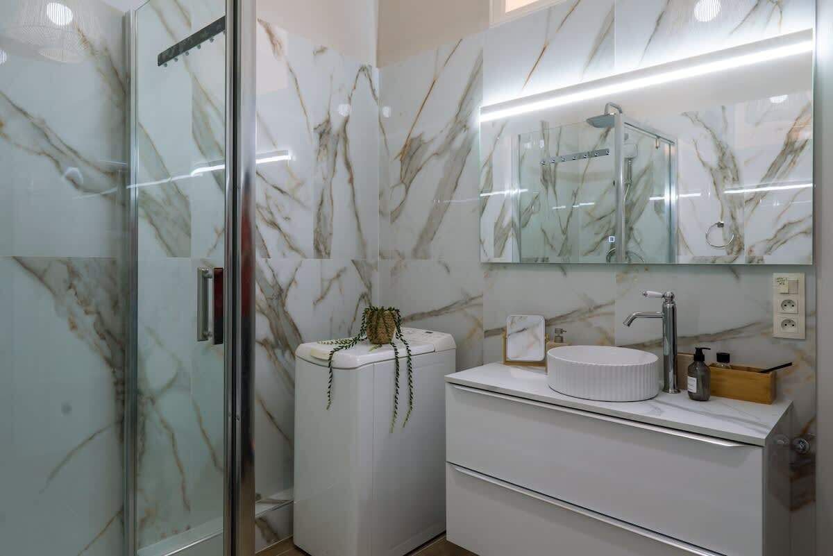 A bathroom with a glass shower enclosure, a white marble vanity, and a mirror above the sink.