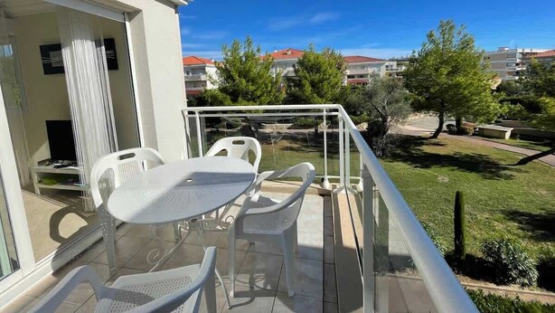 Ein Balkon mit Tisch und Stühlen, der auf eine Grünfläche mit Bäumen und Gebäuden im Hintergrund blickt.