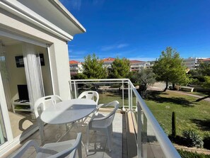 Ein Balkon mit Tisch und Stühlen, der auf eine Grünfläche mit Bäumen und Gebäuden im Hintergrund blickt.