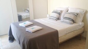 Ein ordentlich bezogenes Bett mit brauner Bettdecke und zwei Kissen, ein Nachttisch mit Lampe sowie ein Spiegel an der Wand.
