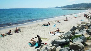 Ein Strand mit Menschen, die sich sonnen und schwimmen, eine felsige Küstenlinie und freie Sicht auf das Meer.