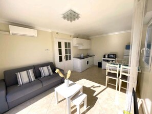 A compact living space with a sofa, a small table, a kitchenette, and a dining area. - L’Escapade Juan Flore, relaxation, family pool (Antibes)